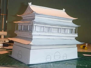 a white model of the drum tower with razor-sharp roof edges, mirrored in a shiny cutting mat